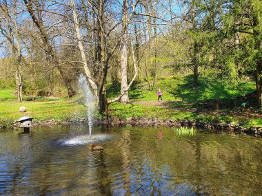 Teich mit Springbrunnen und Frau im Hintergrund, die Nordic-Walking macht