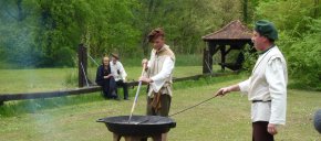 Zwei Männer in historischer Kleidung am Siedekessel beim Salz sieden. Im Hintergrund ein Paar, ebenfalls in historischer Kleidung.