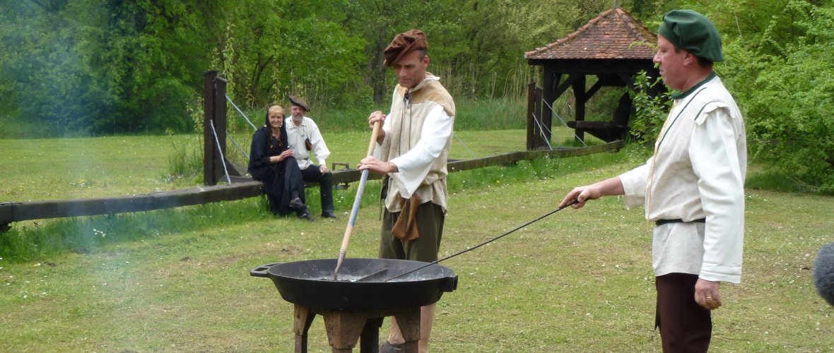 Salzsieder Zwei Männer in historischer Kleidung am Siedekessel beim Salz sieden. Im Hintergrund ein Paar, ebenfalls in historischer Kleidung.