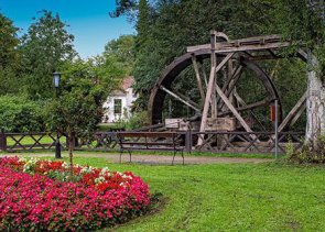 Historisches Wasserrad Historisches Wasserrad aus Holz mit buntem Blumenbeet im Vordergrund