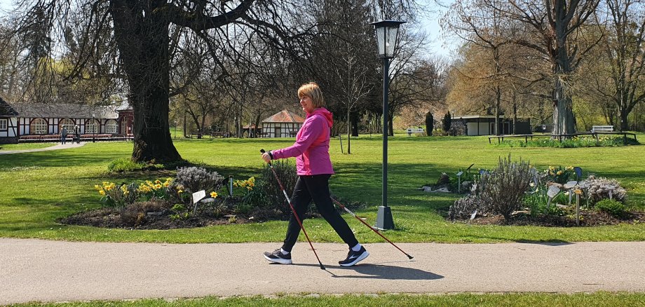 Frau mit Stöcken macht Nordic-Walking in Parklandschaft